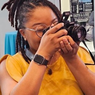 Picture of Dr. Alexus Brown taking a picture with her camera with the word "Services" on top of it to introduce their services through Lexycal Multimedia.